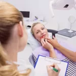 A female patient holding the side of her face while a dentist is writing on a clipboard.