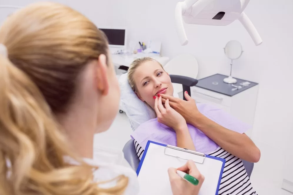 A female patient holding the side of her face while a dentist is writing on a clipboard.