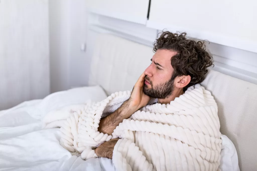 A man is in pain due to a toothache, holding his cheek and looking distressed from the discomfort.