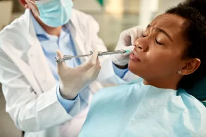 Dentist injecting local anesthetic into female patient's lower gum before oral surgery at Ridge Oral Surgery in New Jersey.