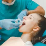Dentist in teal scrubs preparing a patient for oral surgery using a cheek retractor at Ridge Oral Surgery in Basking Ridge, NJ.