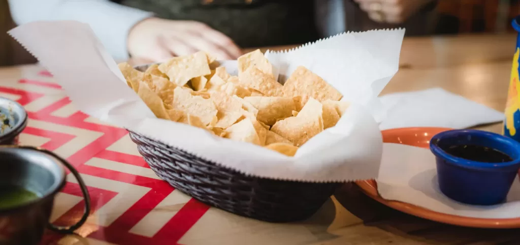 A basket of golden crispy tortilla chips served with a small bowl of spicy salsa, highlighting authentic Mexican cuisine.