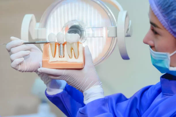 A dental professional in blue gown and mask demonstrates a dental implant model, explaining the process in Basking Ridge, NJ.