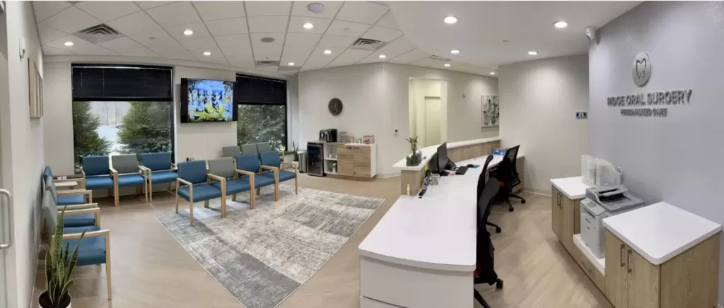 A panoramic view of Ridge Oral Surgery’s waiting room in Basking Ridge, NJ, with modern décor, blue chairs, and a coffee station.