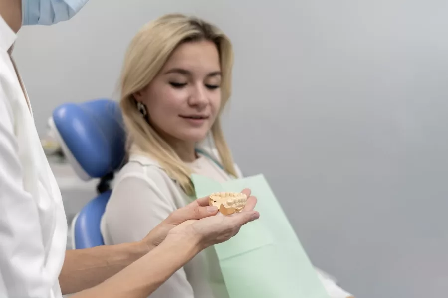 Female dentist explaining wisdom teeth extraction with dental model to patient during consultation at oral surgery clinic.