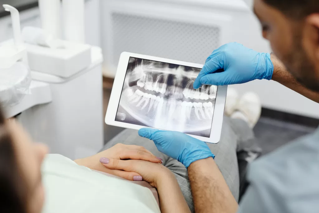 At Ridge Oral Surgery in Baskin Ridge, NJ, a dentist shows a dental X-ray on a tablet in a modern office with medical equipment.