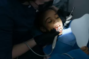 A child in a dentist's chair undergoes a procedure with the dentist using tools, highlighting a calm, professional setting.