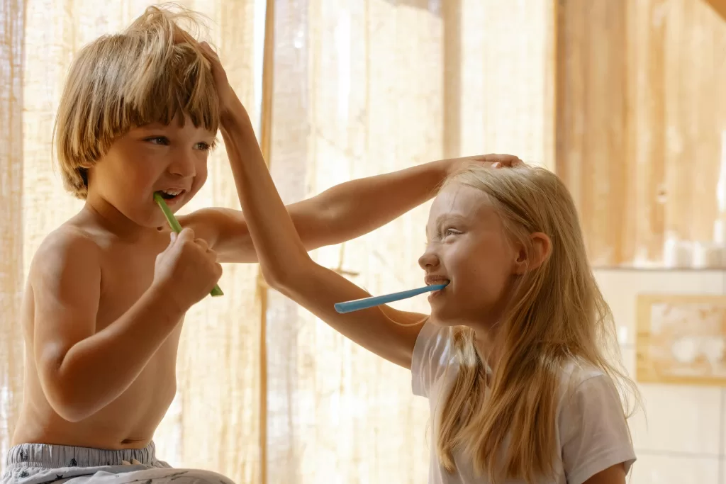 Two children playfully brush their teeth together, highlighting the importance of gentle brushing after tooth extractions for healing.