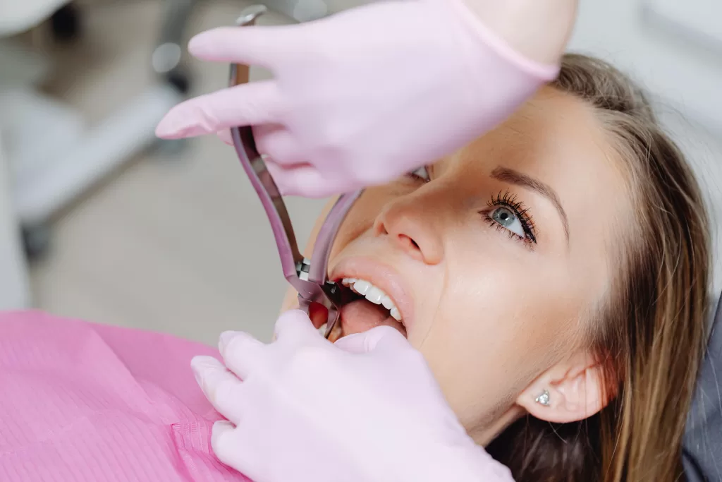 A woman in a dentist's chair undergoes a tooth extraction, with the dentist using forceps, while the patient remains calm.