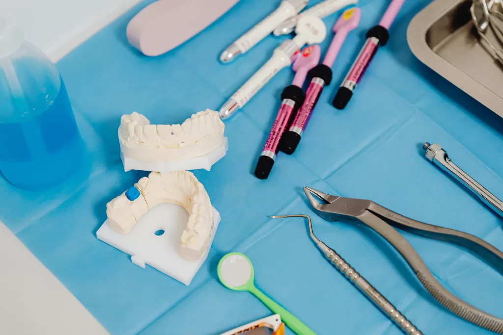 A close-up of dental tools on a blue drape, including a jaw model, syringes, instruments, and blue liquid for post-extraction care.