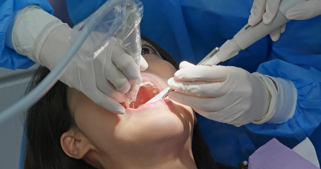 A close-up of a dental procedure, possibly a bone graft and implant on the same day, with a dentist using instruments on the patient's mouth.