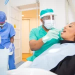 A dental professional in protective gear performing an examination on a patient in a clinical setting at an oral surgery practice in Morristown