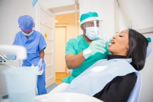 A dental professional in protective gear performing an examination on a patient in a clinical setting at an oral surgery practice in Morristown