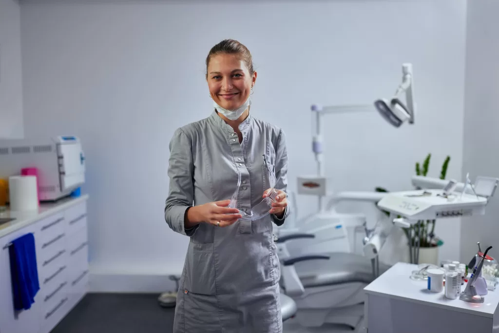 A smiling dentist in a grey uniform standing in a clean clinic environment. Learn flossing tips from dental professionals.