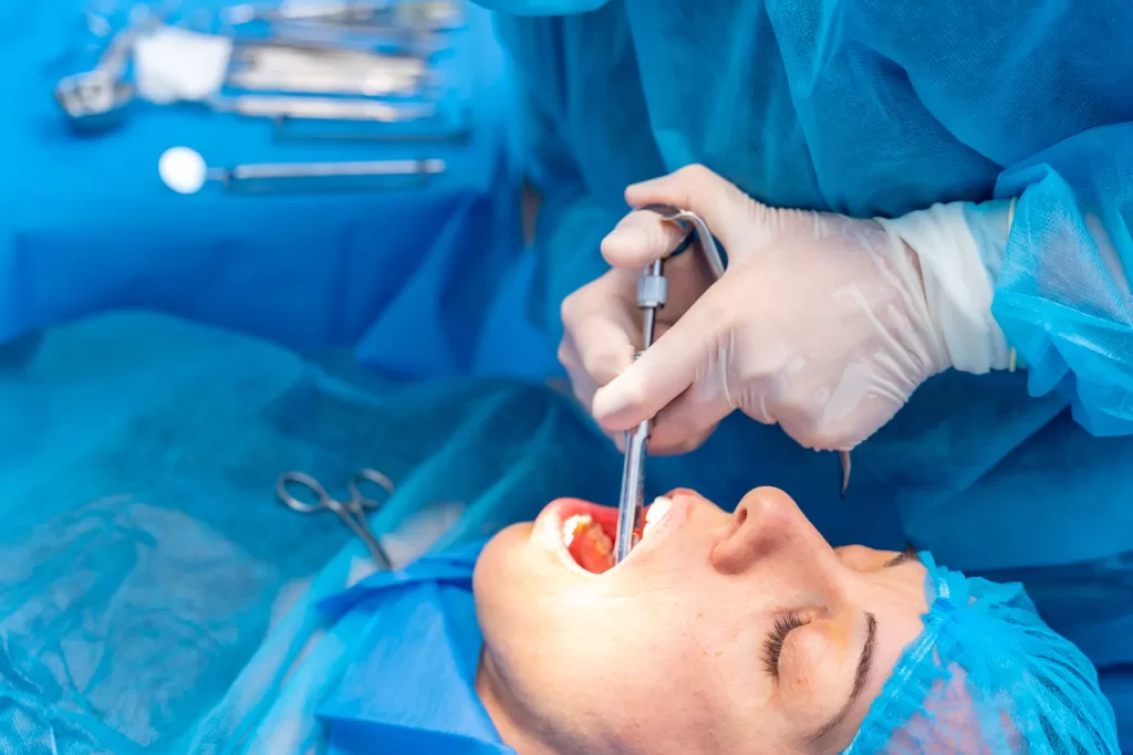 A dentist performing a tooth extraction on a sedated patient in a sterile surgical setup with tools in the background.