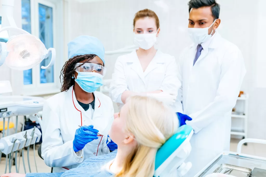 Dentist examining a patient in a dental office with two assistants observing.