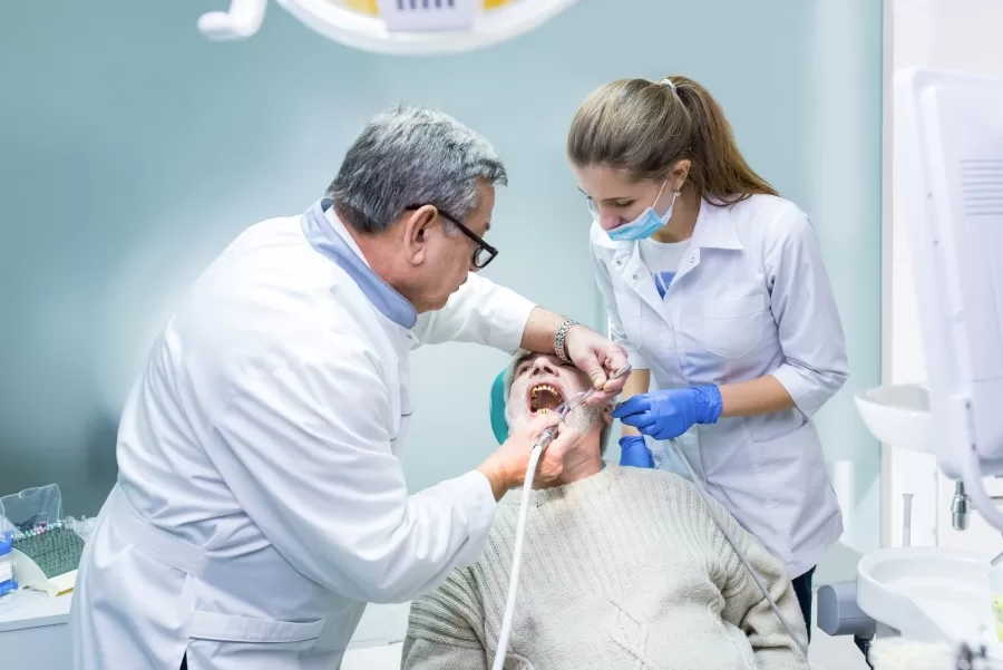Senior dentist and assistant performing a dental procedure on an older male patient in a clinical setting.