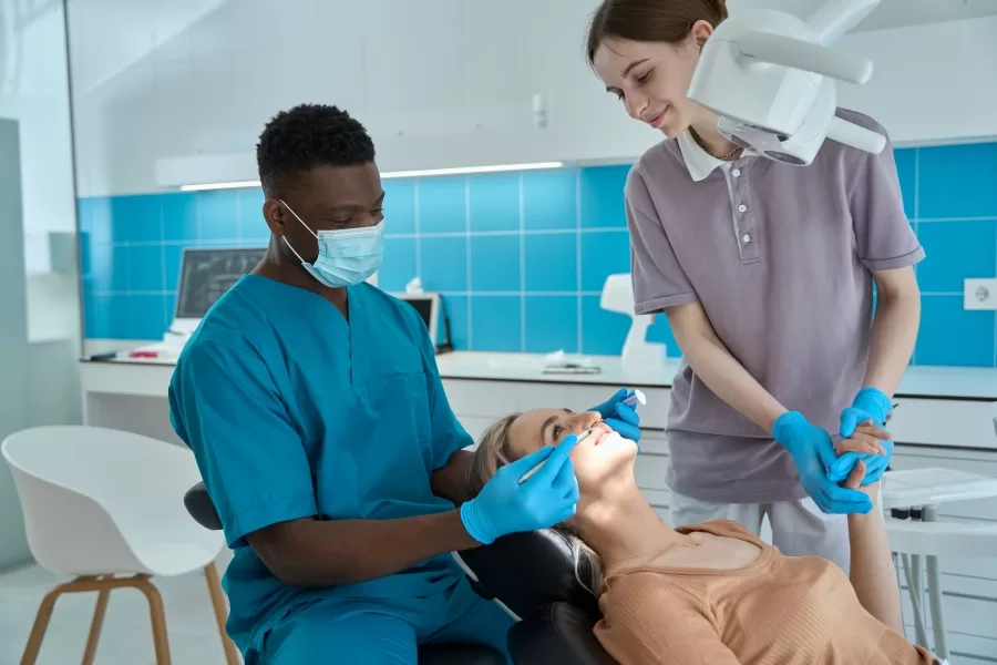 Dental team performing an oral examination on a female patient with modern dental tools and X-ray equipment.