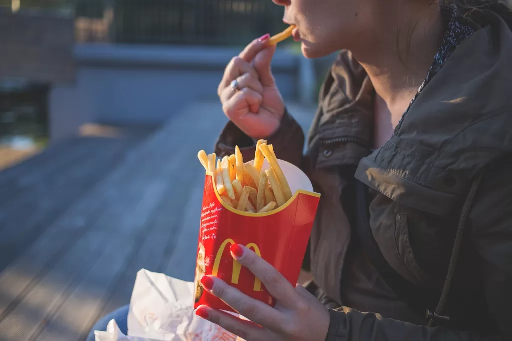 A girl holding Mc Donald's french fries in left hand and eating a fry with right hand