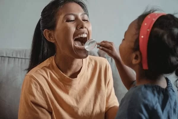 Child pretending to examine a woman’s mouth, imitating oral biopsies.