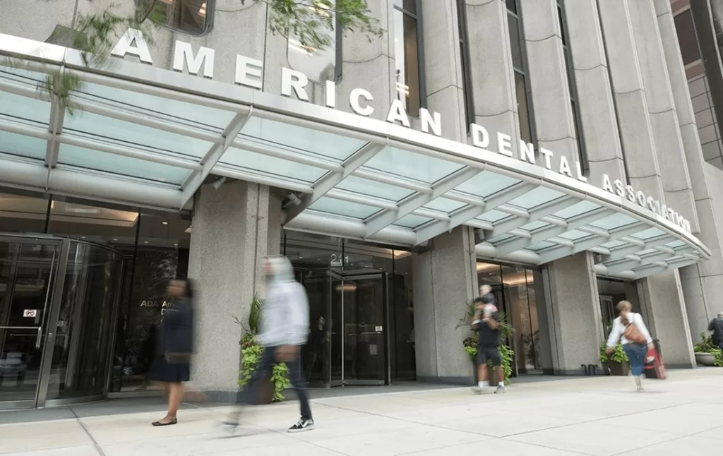 Image of the American Dental Association (ADA) headquarters building with pedestrians walking past the entrance. The ADA supports advancements in dental care, including oral biopsies for diagnosing oral diseases.