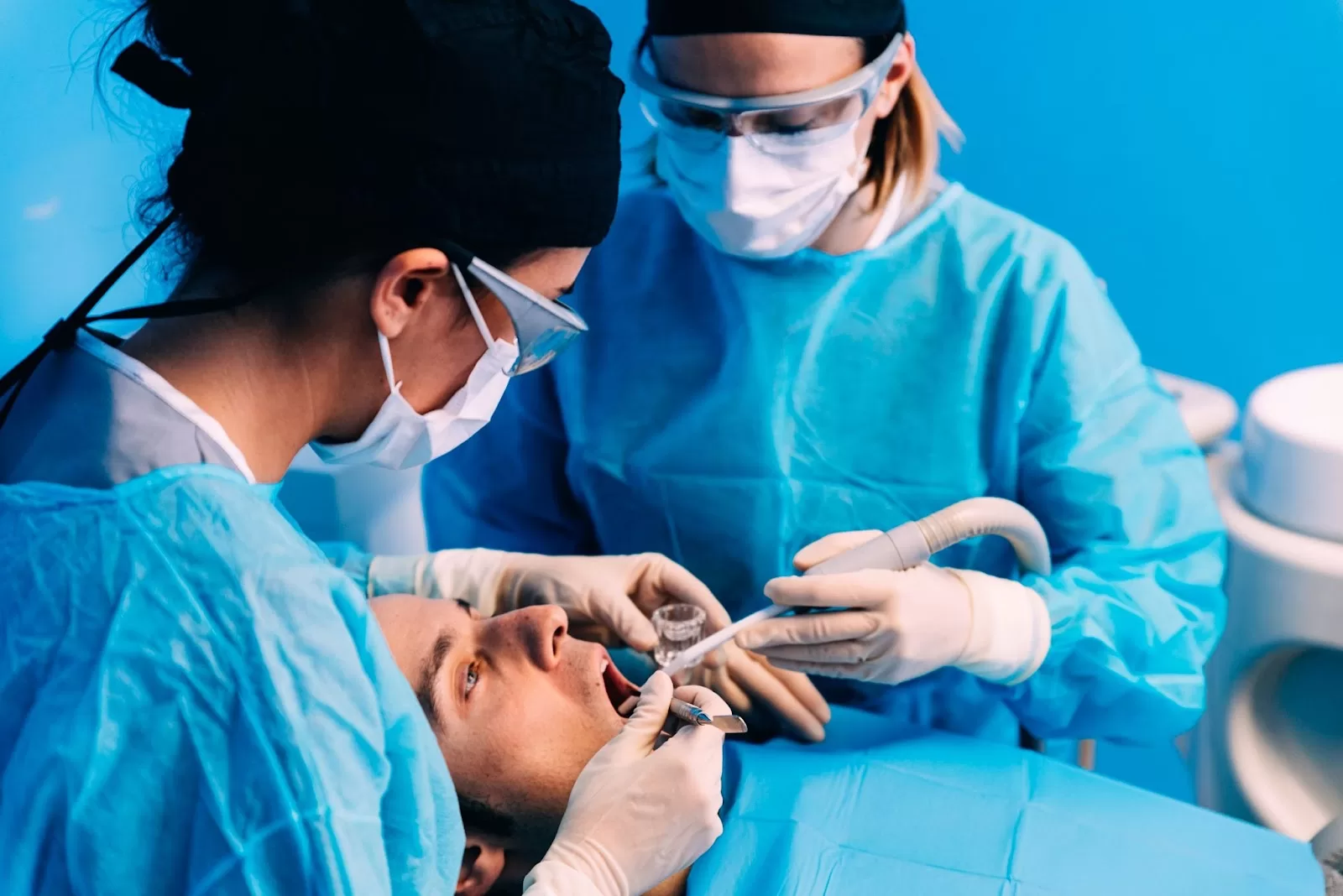 A dentist examines the oral health of a patient through advanced medical equipment. The dentist is assisted by two nurses.