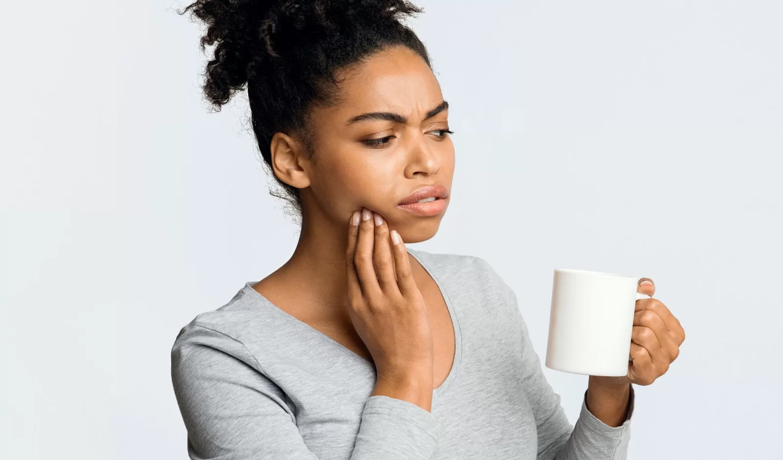 Person experiencing tooth pain while holding a mug, illustrating common dental emergencies and the importance of proper care.