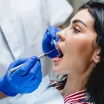 A dentist performs dental surgery on a patient seated in a dental chair, using specialized tools to examine and treat her teeth.