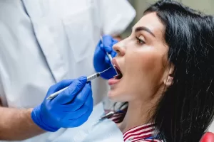 A dentist performs dental surgery on a patient seated in a dental chair, using specialized tools to examine and treat her teeth.