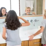 Two children brushing their teeth in front of a bathroom mirror, promoting good oral hygiene habits.