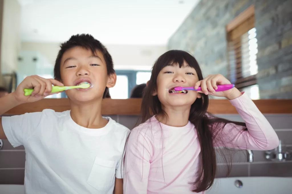 Two children happily brushing their teeth with toothbrushes, demonstrating the importance of oral hygiene in daily routines.