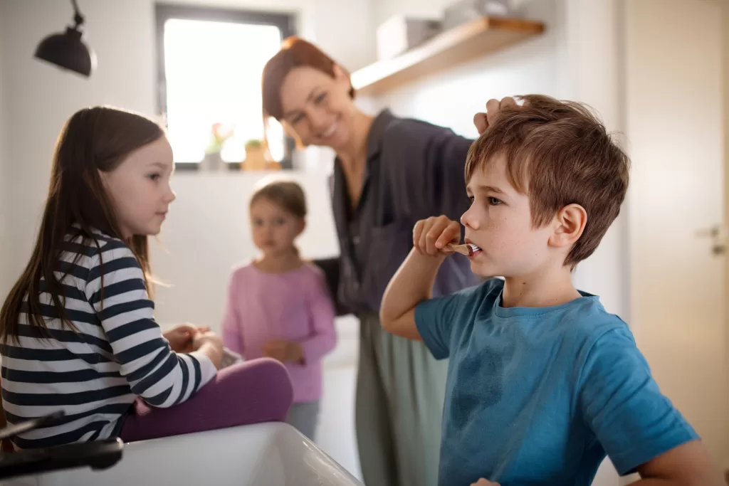  A bathroom featuring a boy brushing his teeth as his siblings and parent look on, emphasizing the importance of oral hygiene routines.