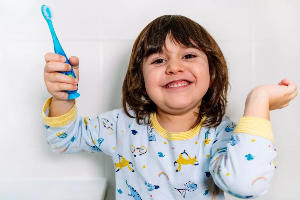  A cheerful child holding a toothbrush while wearing pajamas, celebrating oral hygiene habits with a bright smile.