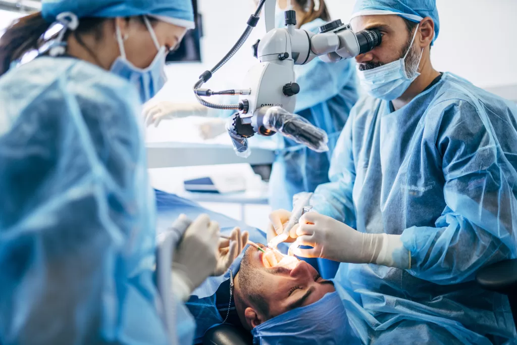 A dentist examines the oral health of a patient through advanced medical equipment. The dentist is assisted by two nurses.