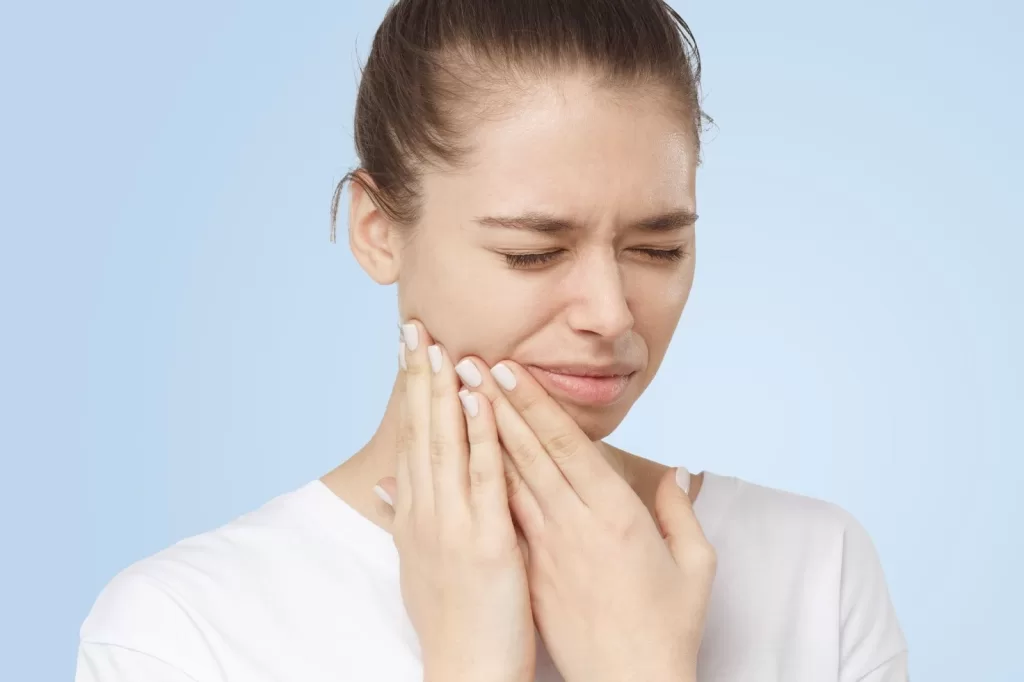 A woman wincing with pain in her teeth, indicating the need for dental surgery,