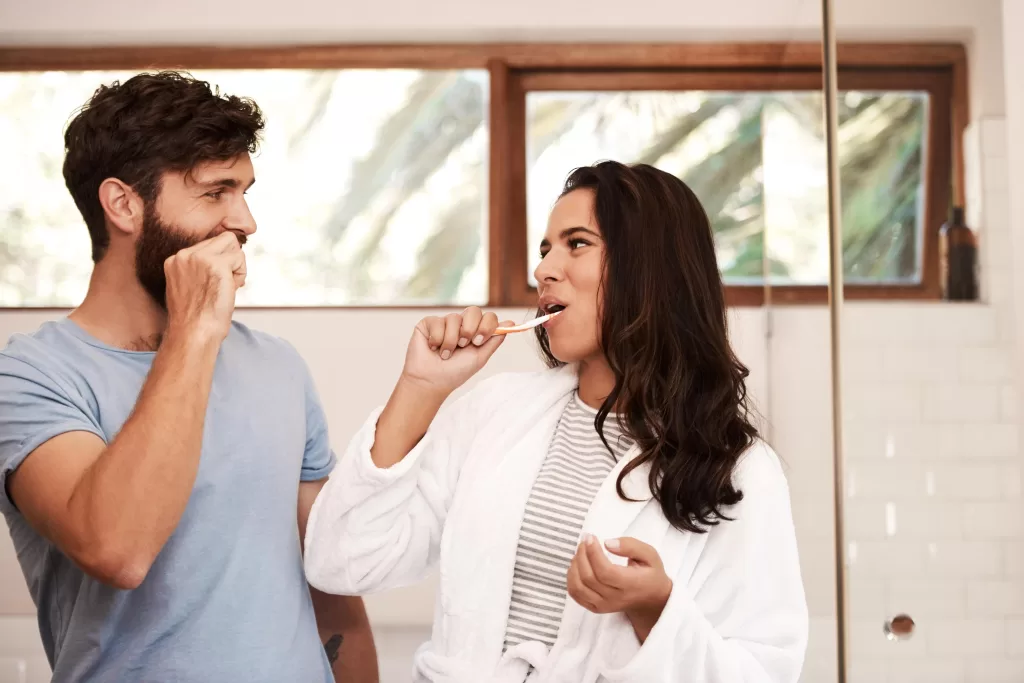 A couple shares a moment while brushing their teeth and taking care of their oral wellbeing.