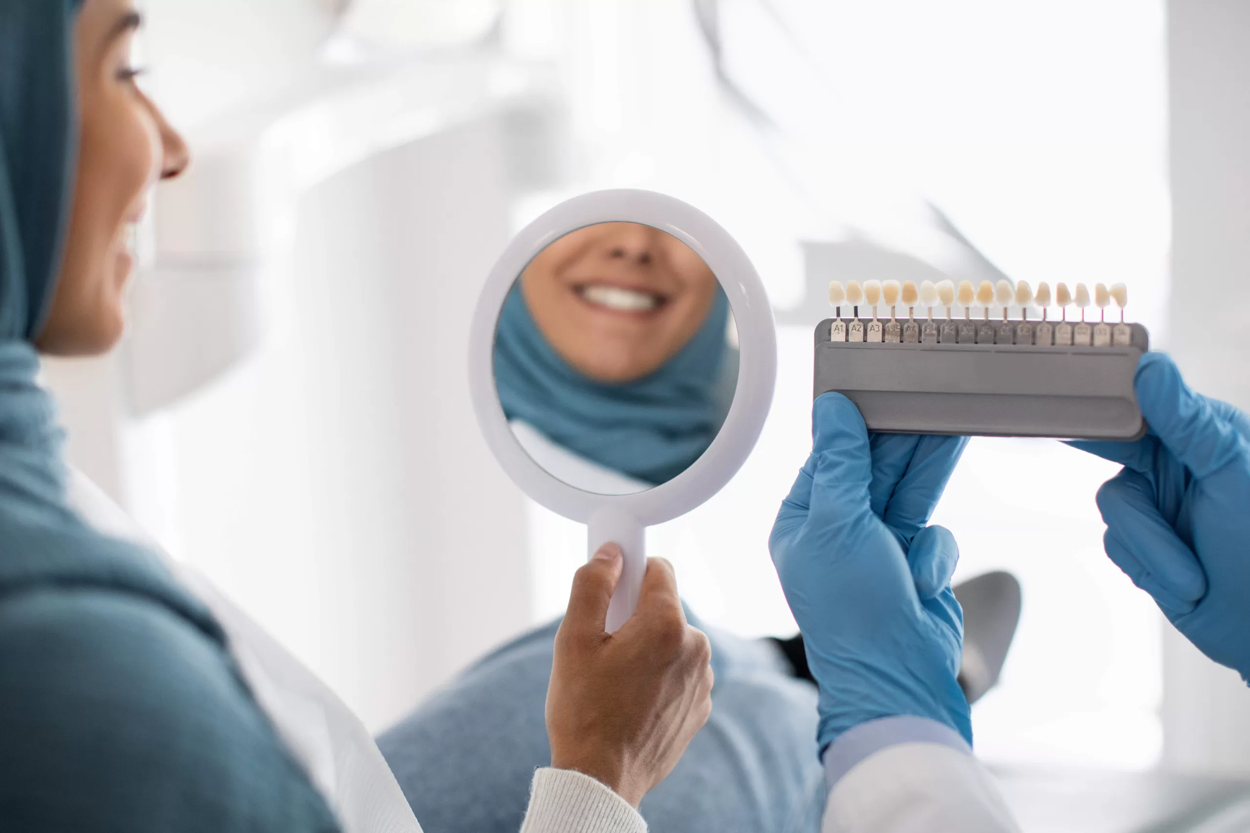 Female Patient Holding Mirror And Looking At Her Smile After Dental Treatment In Stomatologic Clinic
