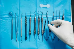 A set of stainless steel dental extraction tools neatly arranged on a blue sterile sheet, with a gloved hand selecting one of the instruments.