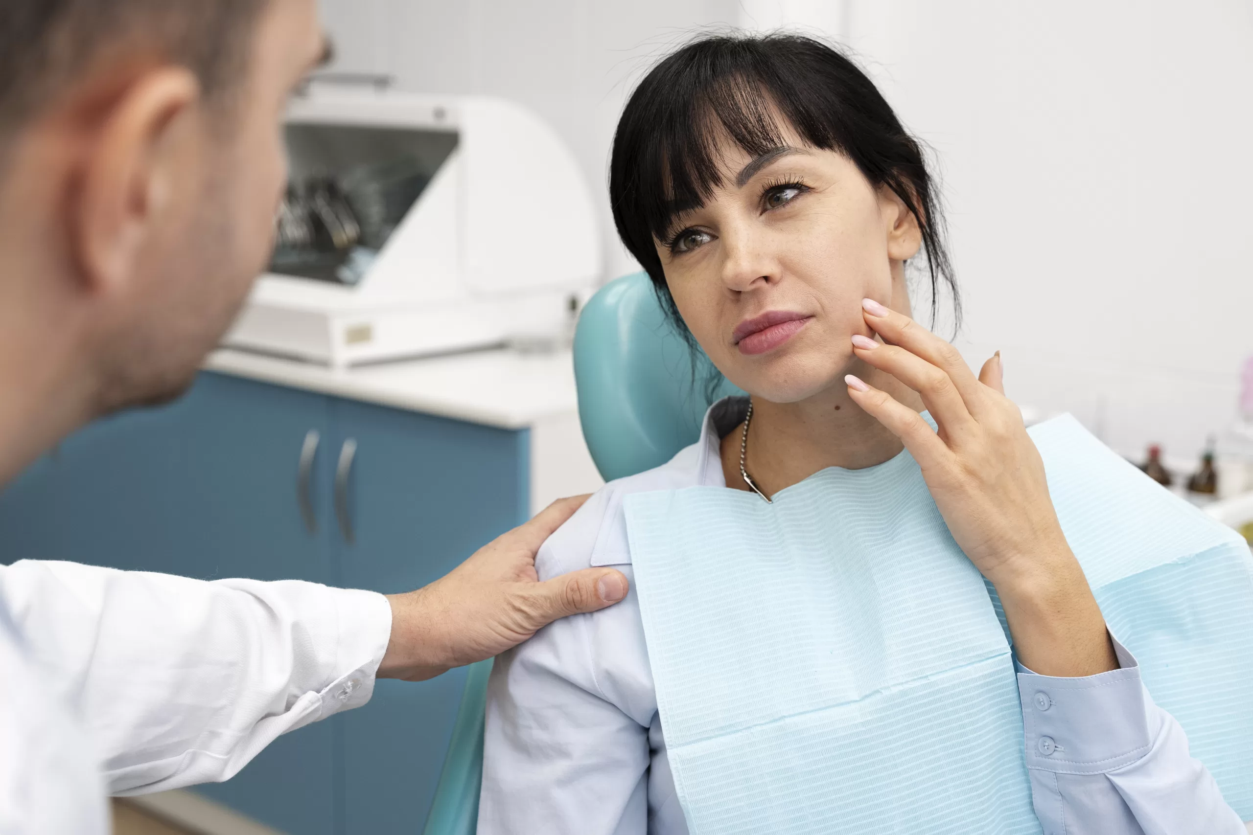 Woman pointing to her jaw to indicate pain during a dental checkup.