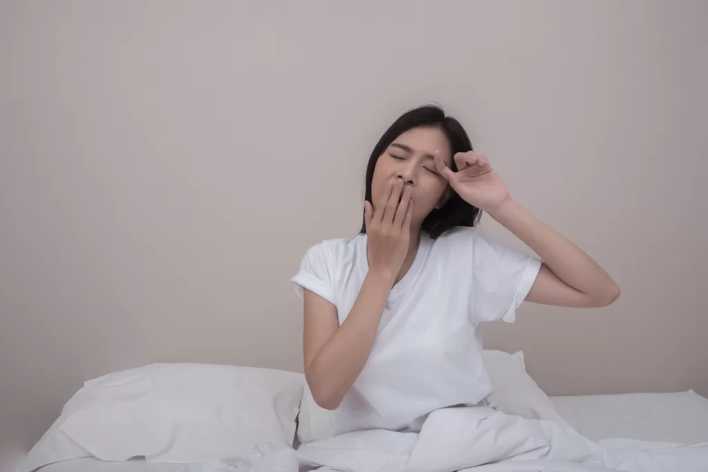 Woman yawning and stretching in bed, feeling tired after sleep.
