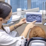 A dentist showing a patient a dental X-ray in a dental clinic, surrounded by surgical instruments.