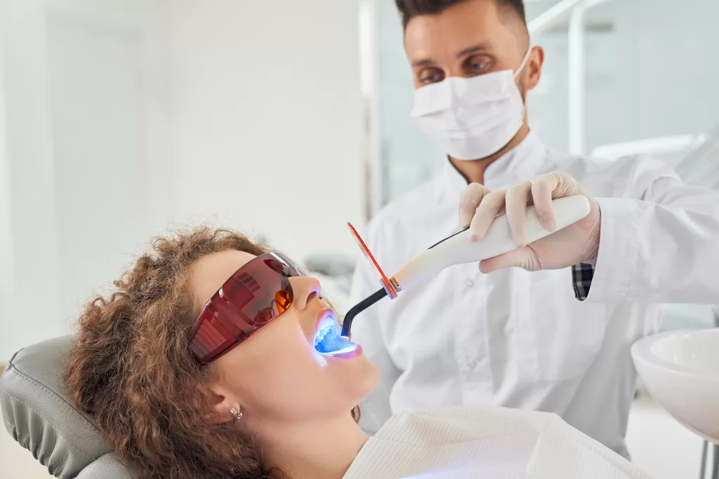 A girl lying on a chair while a dentist uses an ultraviolet tool in her mouth at the Ridge Oral Surgery clinic.