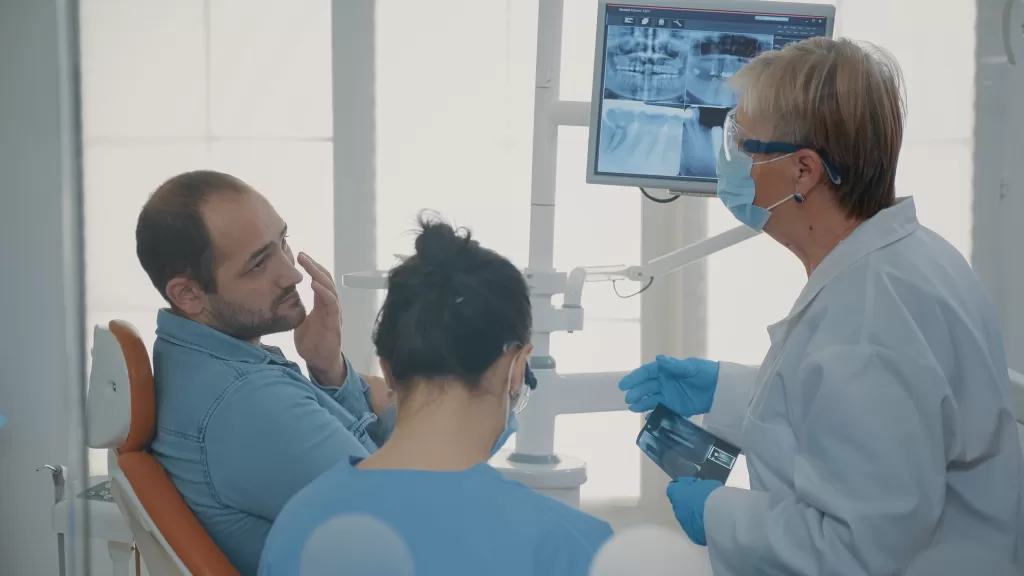 A dentist and a nurse explain a dental X-ray scan to a patient with a toothache in a dental clinic.