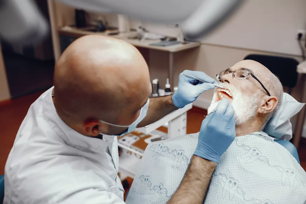 A dentist examines an elderly male patient’s mouth during a dental procedure.