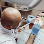A dentist examines an elderly male patient’s mouth during a dental procedure.