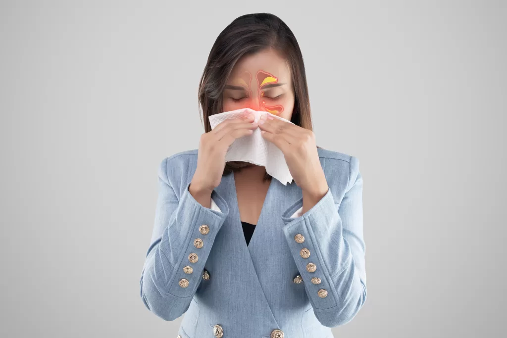 A woman in a blue blazer sneezes into a napkin due to sinus symptoms.