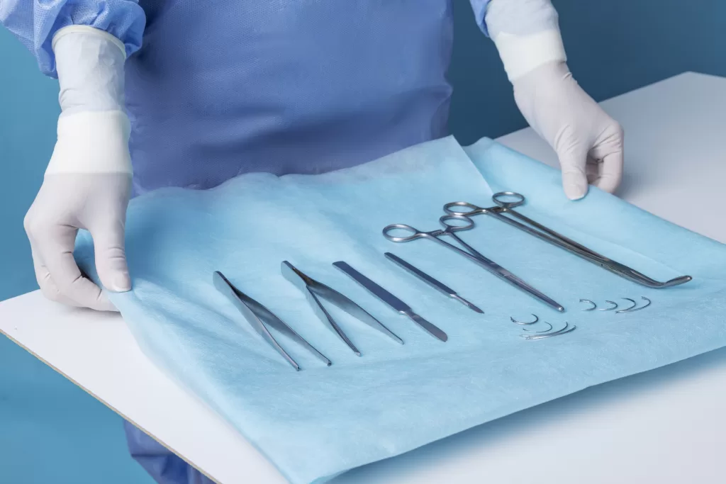 A dentist laying out a tray of surgical instruments on a white table.