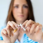 Close-up of a woman snapping a cigarette in half, symbolizing quitting smoking before oral surgery.