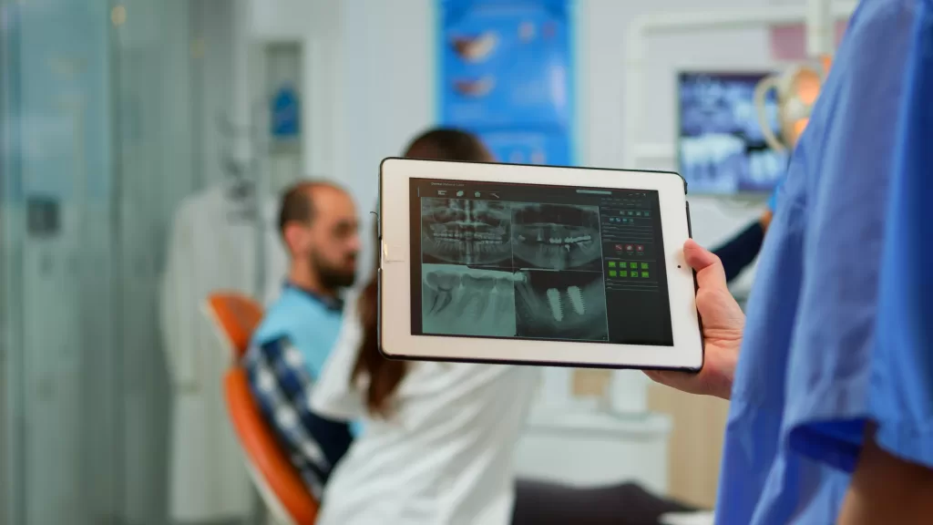 A close-up of a dentist holding a tablet with digital radiography, while the doctor is checking up on a patient.