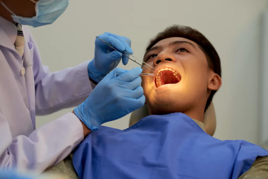 A man sitting with his mouth wide open and being examined by a dentist at the Ridge Oral Surgery clinic.